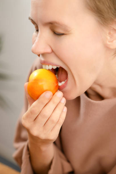 elegancia fructífera: una seductora mujer de mediana edad disfruta de una ciruela amarilla madura, saboreando la bondad afrutada de su bocadillo - plum yellow eating beauty and health fotografías e imágenes de stock