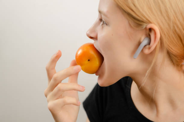 golosina saludable para adolescentes: una joven delgada disfruta de la bondad de una ciruela amarilla madura, saboreando el deleite saludable de su bocadillo afrutado - plum yellow eating beauty and health fotografías e imágenes de stock