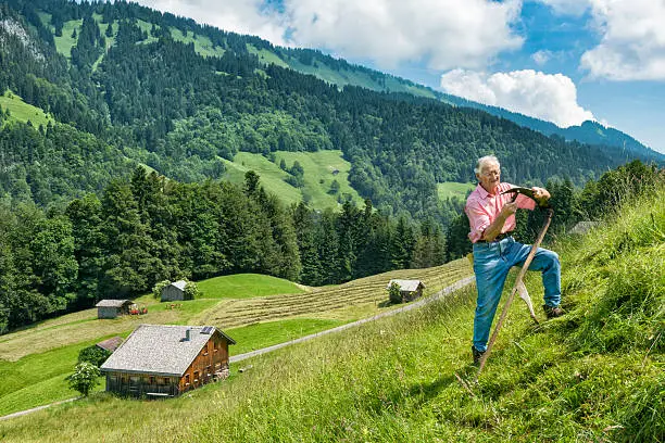 senior mountain farmer sharpening a scythe for mowing a steep meadow in the austrian alps,  Bregenzerwald, Vorarlberg