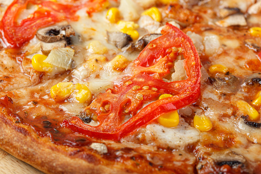 delicious pizza with chicken, mushrooms, cheese, tomatoes and corn on a wooden background close-up