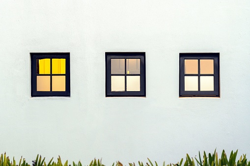 Four windows in two different styles mounted on the side of a white brick building against a clear blue sky