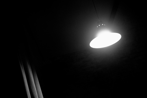 An illuminated lamp in a darkened room, with curtains silhouetted in the shadows