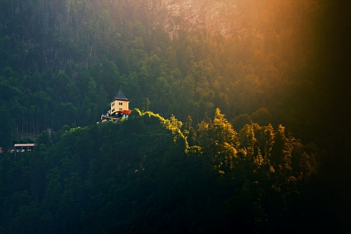 An aerial view of a secluded house perched atop a lush, tree-covered mountain, surrounded by natural beauty