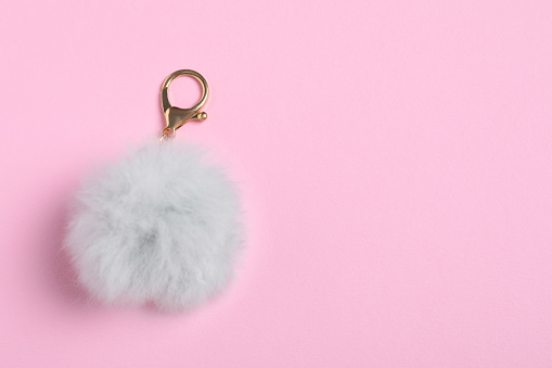 Gray fur keychain on pale pink background, top view. Space for text