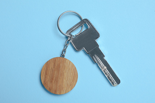 Key with wooden keychain in shape of smiley face on light blue background, top view
