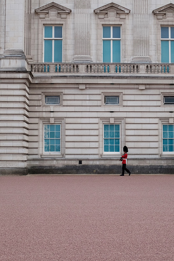 A member of the King's Guard wearing the iconic Bearskin Hat marches past a window of Buckingham Palace.