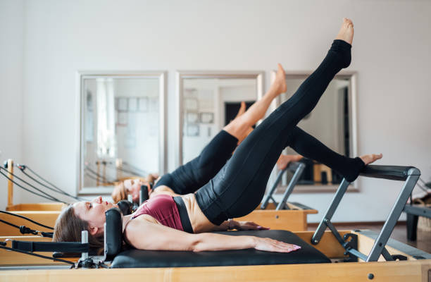 istock Two fit-shaped females doing bridge exercise with raised leg static core muscles exercise using pilates reformer machine in the sport athletic gym with a mirror wall. Active people training concept 1791705021