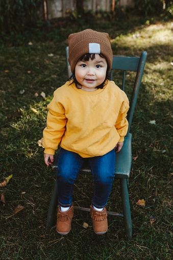 An adorable Native American two~year~old girl, sitting on a little chair outside.