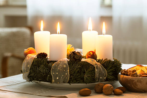 advent wreath burning candle at christmas time advent wreath on table, 4 candles burning, bowl with nuts and dried apples at the right, healthy snack for christmas time advent candle wreath adventskranz stock pictures, royalty-free photos & images