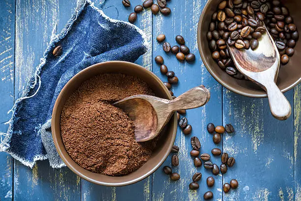 Photo of Bowls of uncut and ground coffee beans on blue wooden table