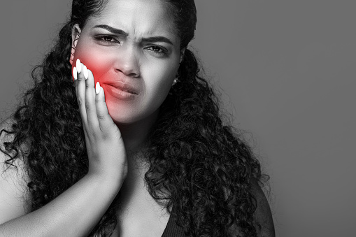 Black and white photo of latin chubby lady suffering from tooth pain, touching sore red zone on her cheek, isolated on studio background, copy space