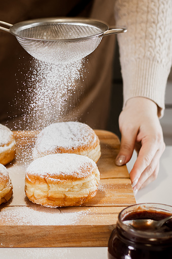 Woman chef prepares fresh donuts in her bakery. Cooking traditional Jewish Hanukkah Sufganiyot. Small business concept. Hands sprinkle Berliners with powdered sugar.