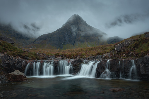 Morning view of a river with a waterfall and a cloud-shrouded mountain peak. Scenic landscape with trickling waterfall in the morning. Fairy Pools, Isle of Skye, Scottish Highlands, UK