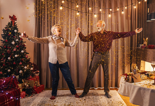 An excited grandparents dancing and celebrating christmas and new year at cozy home.