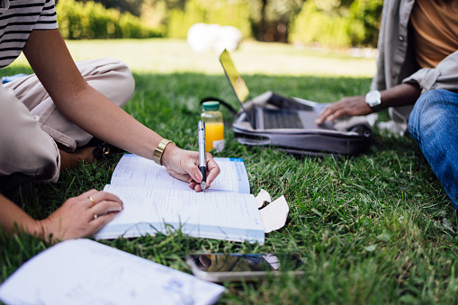 A side view of two unrecognizable multiethnic students (African-American and Caucasian one) studying outdoors. (defocused)