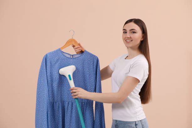 istock Woman steaming blouse on hanger against beige background 1791815496