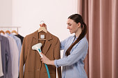 Woman steaming jacket on hanger in room