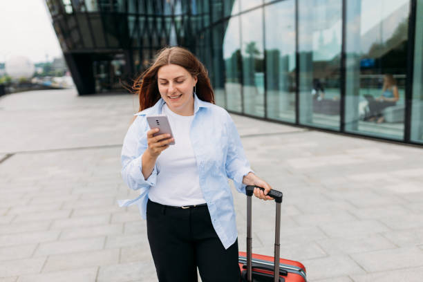 istock Elegant businesswoman checking e-mail on mobile phone while walking with suitcase outside airport. Beautiful 30s woman searching information on the internet with smartphone outdoors 1791821766