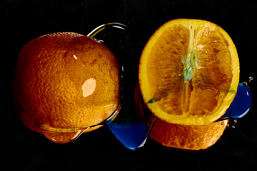 Two halves of an orange against a black background covered in honey with blue food colouring