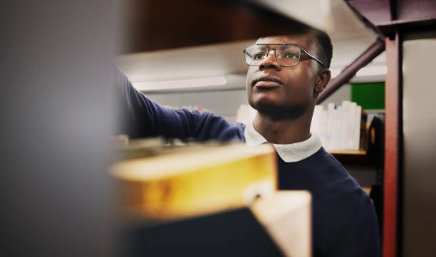 istock Knowledge, research and black man in a library search and learning on campus for studying and education in college. Smart, clever and young person in an academy with books on a shelf for an exam 1791833355
