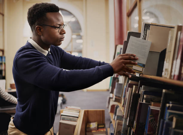 istock University, research and man in a library reading and learning on campus for knowledge and education in college. Smart, clever and young person in an academy with books on a shelf for an exam 1791833361