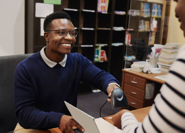 istock Happy librarian man, scan books and help desk for learning, knowledge and administration with technology. African people, library employee and receptionist for study, information and education 1791833568