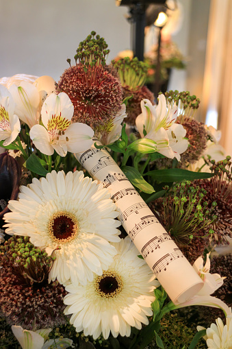 Flower arrangement with white Gerbera and Peruvian lily (Alstroemeria) and a rolled sheet of music