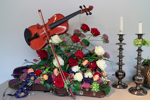 Rose flower arrangement in a violin case with a violin, violin bow and candlesticks