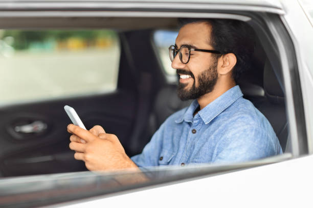 istock Happy eastern man in casual going by taxi, using smartphone 1791850395