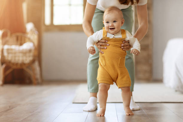 heureux petit garçon faisant ses premiers pas à la maison avec sa mère - bébé qui marche photos et images de collection