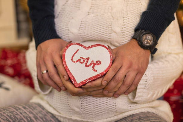 A close-up shot of hands creating a heart shape over a pregnant woman's belly, symbolizing love and anticipation.