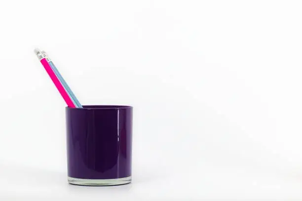 A violet glass desktop organizer on a white backdrop contains three pencils with erasers in pink, blue, and navy hues.