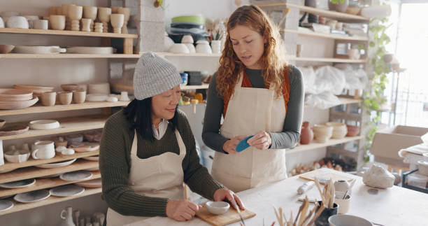 istock Pottery, art and teacher with student in a workshop for learning with clay sculpting or molding. Creative, teaching and artist manufacturing a mud ceramic design product with mentor in a studio. 1791907617