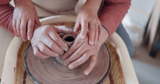 istock Art, hands and clay on wheel together, help with container or bowl in studio, workshop or pottery class. Artist, teacher and student with creative, unique mold or shape for ceramic product design. 1791907641