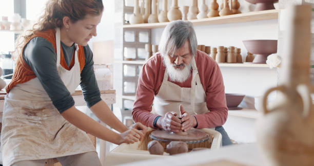 istock Pottery, wheel and teacher with student in workshop for art learning with clay sculpting or molding. Creative, teaching and artist manufacturing a mud ceramic design product with mentor in a studio. 1791907642