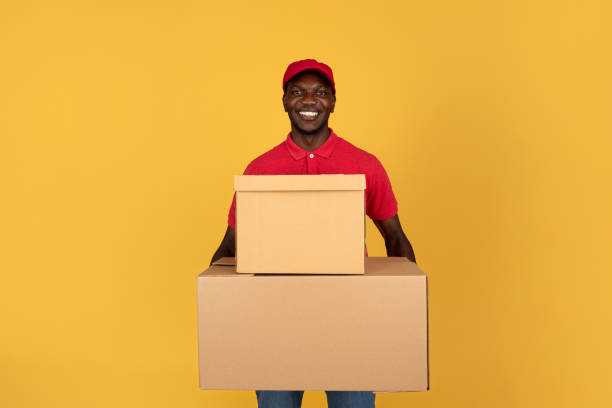 istock Glad handsome millennial black guy courier in red uniform hold many big boxes for delivery 1791919952