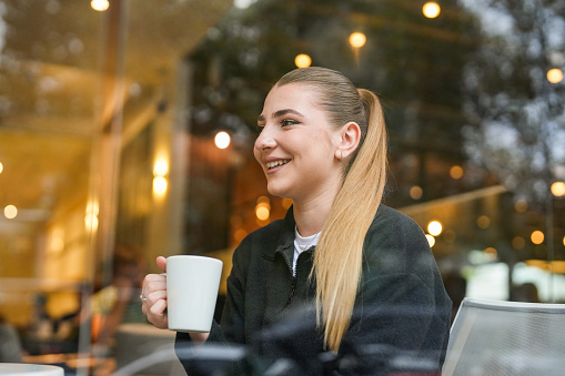 Female student sitting in the cafe drinking coffee from a coffee cup in her hand