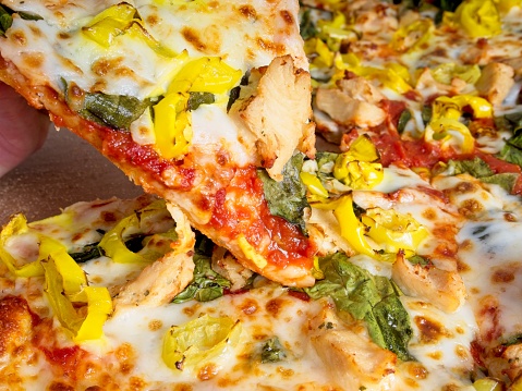 Cheesy taste sensation, a fresh slice of pizza being pulled away from the pie. Mozzarella cheese pizza with hot peppers, chicken and spinach fresh from the pizza shop.
