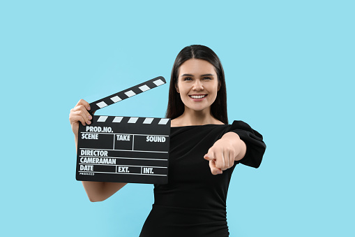 Young woman holding a movie clapboard over black background, studio shot