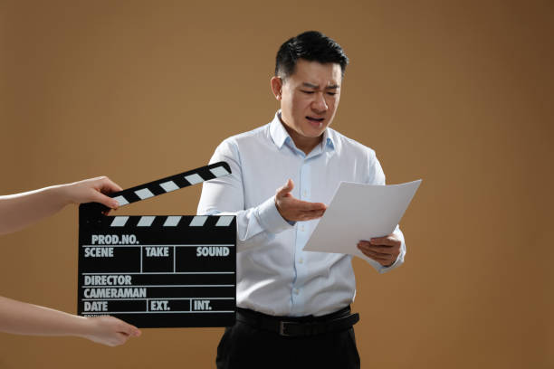 istock Emotional asian actor performing role while second assistant camera holding clapperboard on brown background. Film industry 1791950328