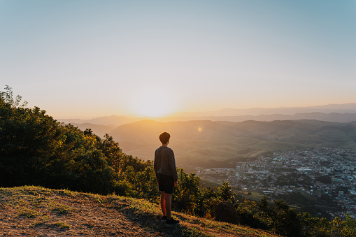 Teenage boy watching the sunset on top of the mountain