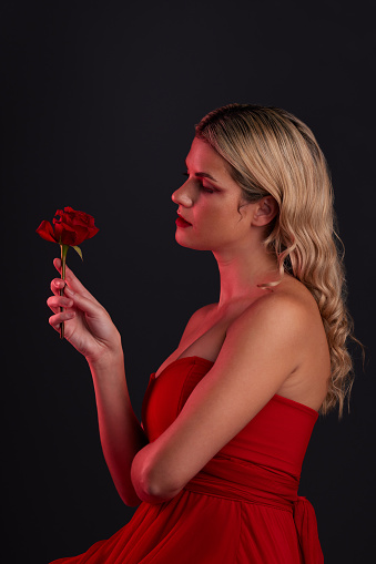 Beauty, fashion and woman with a rose on a dark, black background in a studio thinking of love, romance or red aesthetic. Girl with a flower, dress and formal style in fantasy, fairytale or art