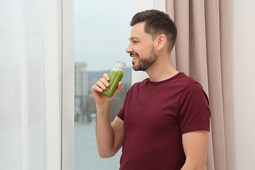 Man drinking delicious fresh smoothie indoors, space for text