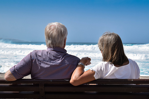 Las Américas, Tenerife, Spain February 12, 2023 -Senior couple sitting on a wooden bench on the beach of Tenerife and looking at the Atlantic Ocean