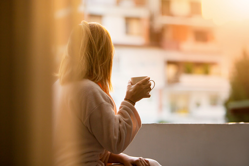 Embrace the serenity of a new day with this captivating image of a woman seated on her balcony, basking in the first light of dawn. Savoring a cup of coffee, she exudes calmness and relaxation, poised to tackle the day ahead. The sun bathes the scene in a warm glow, casting a tranquil atmosphere as she prepares for work. This picture captures the essence of a peaceful morning, where the blend of coffee, sunshine, and a moment of quiet reflection sets the perfect tone for a day filled with productivity and enjoyment.