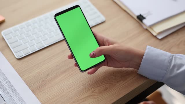 Woman holding smartphone with green screen in office