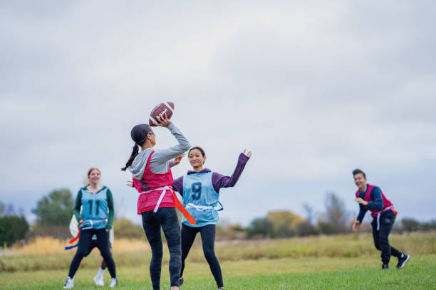 A group of University students run around on a field as they play a game of flag football together.  They are each dressed comfortably and have numbered team pinnies on.