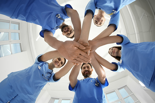 Young doctors stacking hands together indoors, bottom view