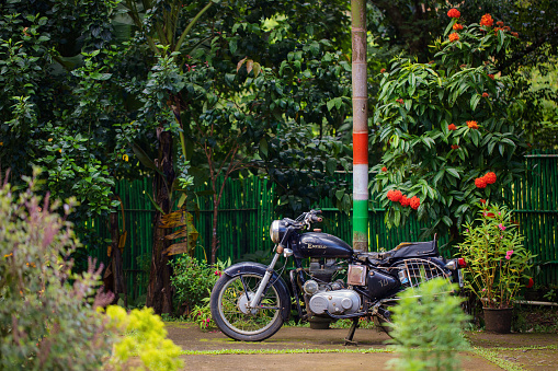 Nilambur, India - October 13, 2023. A Royal Enfield motorcycle is parked by a telephone pole painted with the colours of the Indian flag.