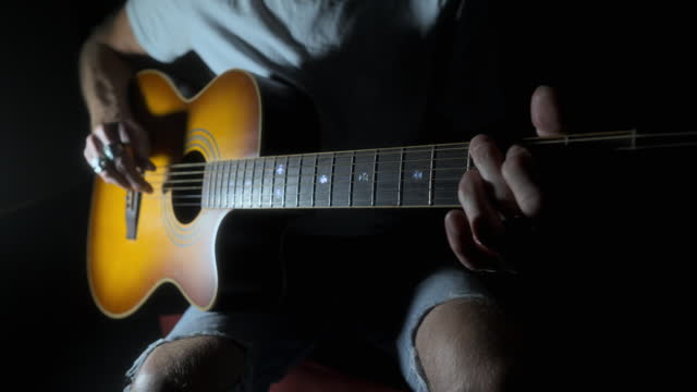 Man with missing fingers playing acoustic guitar in strong moody lighting. Quarter stop pro mist filter. 60fps.
